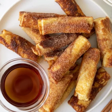 Delicious French Toast Roll-Ups served with syrup and berries on a plate