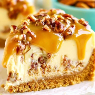 Slice of decadent Pecan Praline Cheesecake topped with nuts and caramel drizzle.